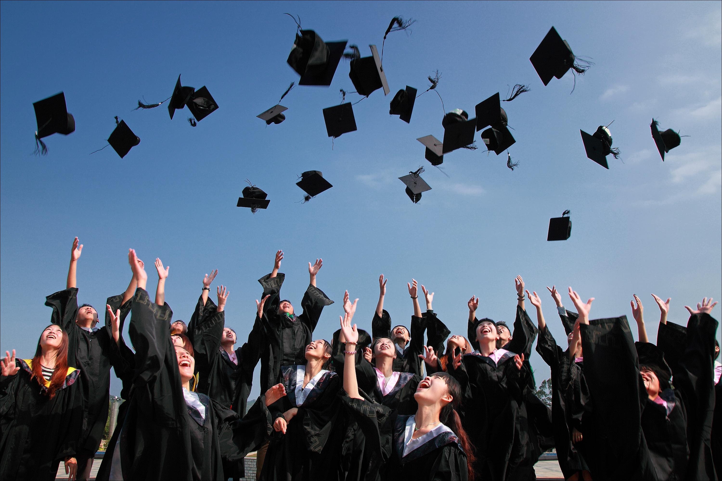 Masters degree graduates tossing graduation caps in the air